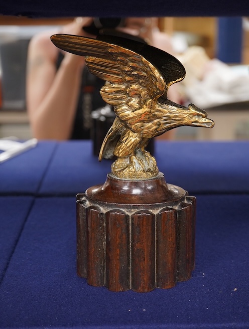 Two brass car mascots in the form of eagles, one mounted on a threaded radiator cap, the other mounted on a wooden base, the larger with a wingspan of 31cm. Condition - fair, one eagle with bent wing.